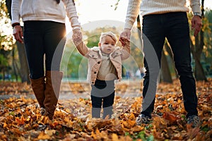 Little boy is holding hands of the parents. Standing in the autumn park