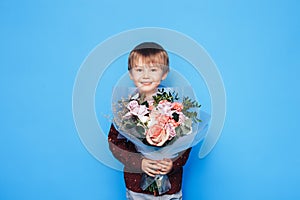 Little boy holding a large bouquet of roses in his hands against a blue background. Valentine`s Day. Mother`s day