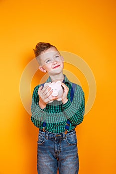 Little boy holding a piggy bank in his hands on yellow background