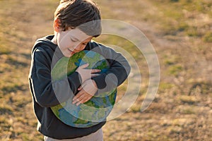 Little boy holding planet in hands against green spring background. Earth day