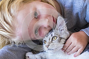 Little boy holding and playing with kitten in living room at home. Portrait of boy holding neck of young cat. Close up of face of