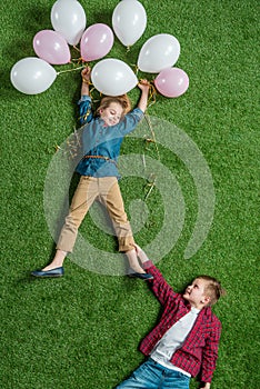 Little boy holding smiling girl with balloons on grass