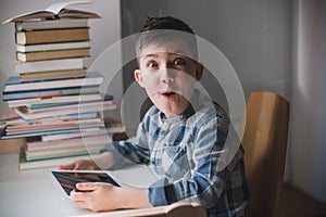 Little boy is holding a tablet and looks suprised.