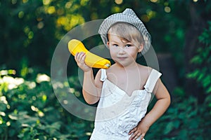 Little boy holding yellow zucchini squash in summer garden farmer boy in white casual robe and hat