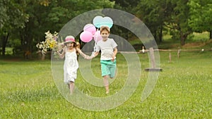 Little boy holds the girl by the hand and they run along the lawn together. Slow motion