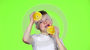 Little boy holds an orange slice and makes various grimaces. Green Screen. Slow motion