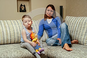 A little boy holds a toy and lying on sofa by his mother. Happy family resting at home.