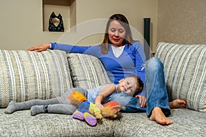 A little boy holds a toy and lying on sofa by his mother. Happy family resting at home.