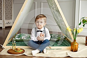 A little boy in holiday clothes is sitting in a tent in his room