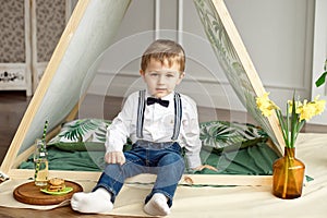A little boy in holiday clothes is sitting in a tent in his room