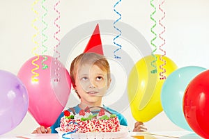Little boy in holiday hat with festive cake and balloons