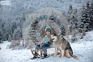 Little boy hug dog and having fun in the snow. Winter travel kid.