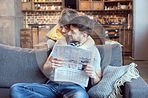 Little boy hugging father reading newspaper at home