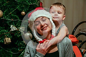 A little boy hugging his mom wearing Snow Maiden hat sitting on background of New Year tree, blur and grain effect.