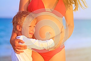 Little boy hugging pregnant mother tummy at beach