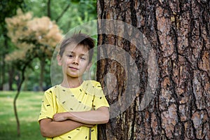 Little boy hugs a tree trunk - children love the nature, sustainability concept. Happy smiling kid look directly to camera. Save