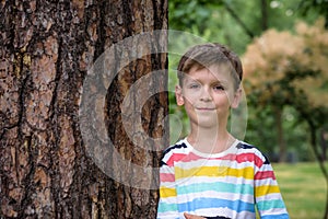 Little boy hugs a tree trunk - children love the nature, sustainability concept. Happy smiling kid look directly to camera. Save