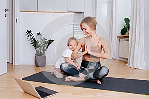 Little boy hugs woman doing yoga on a yoga mat in front of a laptop at home