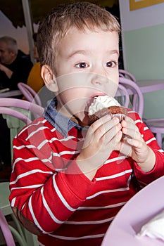 Little boy hungrily eat chocolate cupcake in a cake shop