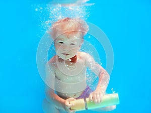 Little boy infant with red butterfly diving underwater in swimming pool, learn to swim.