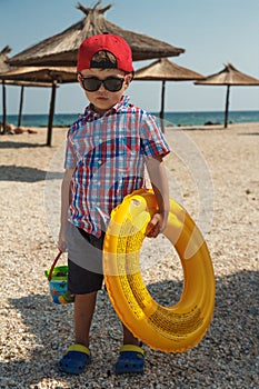 A little boy with an inflatable circle for swimming in glasses on the beach near the sea.