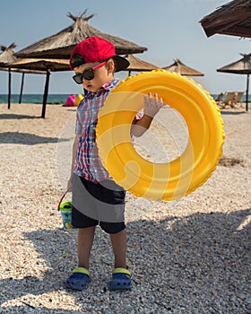 A little boy with an inflatable circle for swimming in glasses on the beach near the sea.