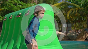 Little boy on an inflatable obstacle course in an aqua park. Summer concept. Slowmotion shot