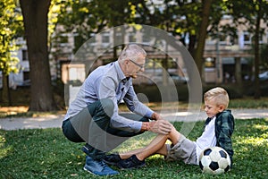 Little boy with injured leg getting plaster from grandfather outdoors in park.