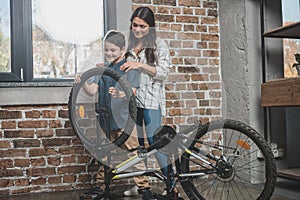 Little boy installing a new wheel onto his bicycle while his mother is standing
