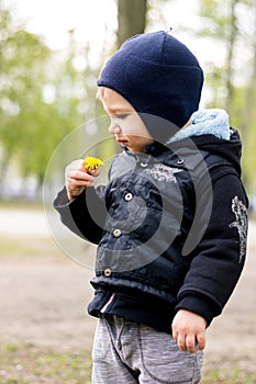 A little boy istands turning sideways and sniffing a flower crooks his face.