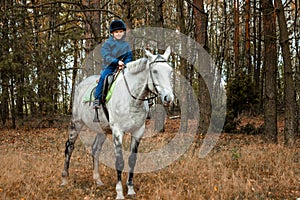 Little boy in a jockey cap on a white adult horse on a background of nature. Jockey, hippodrome, horseback riding