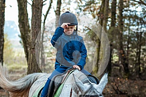 Little boy in a jockey cap on a white adult horse on a background of nature. Jockey, hippodrome, horseback riding