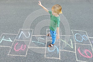 Little boy jumping by hopscotch drawn on asphalt. Child playing hopscotch game on playground on spring day. Top view