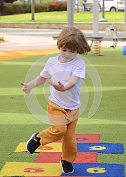 Little boy jumping by hopscotch drawn. Boy playing hopscotch game on playground on spring day.