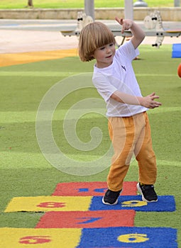 Little boy jumping by hopscotch drawn. Boy playing hopscotch game on playground on spring day.