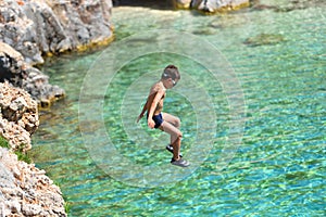 Little boy jumping off cliff into the ocean. Summer fun lifestyle. Brave kid