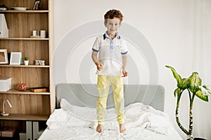 A little boy jumps on his bed in the bedroom and laughs.