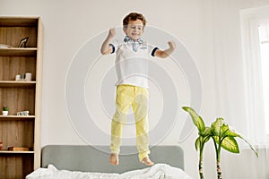 A little boy jumps on his bed in the bedroom and laughs.