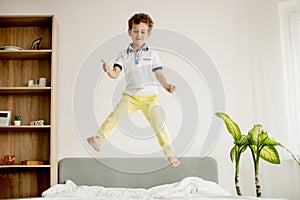 A little boy jumps on his bed in the bedroom and laughs.