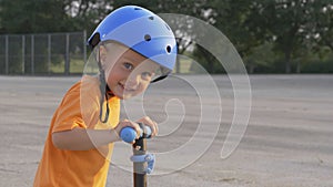 Little boy kid, child in orange t-shirt and blue helmet is riding scooter. Childhood memories, safe and funny experience .