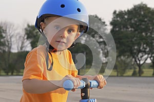 Little boy kid, child in orange t-shirt and blue helmet is riding scooter. Childhood memories, safe and funny experience .