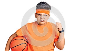 Little boy kid holding basketball ball annoyed and frustrated shouting with anger, yelling crazy with anger and hand raised