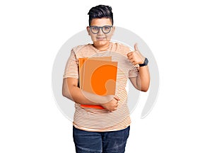 Little boy kid holding book wearing glasses doing happy thumbs up gesture with hand