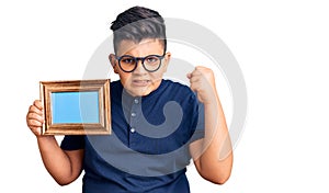 Little boy kid holding empty frame annoyed and frustrated shouting with anger, yelling crazy with anger and hand raised