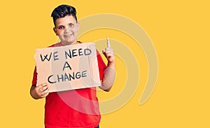 Little boy kid holding we need a change banner surprised with an idea or question pointing finger with happy face, number one