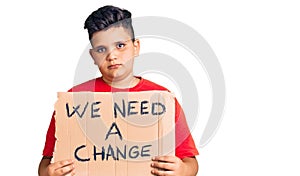 Little boy kid holding we need a change banner thinking attitude and sober expression looking self confident