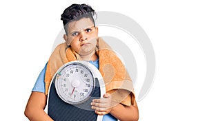 Little boy kid holding weight machine to balance weight loss thinking attitude and sober expression looking self confident