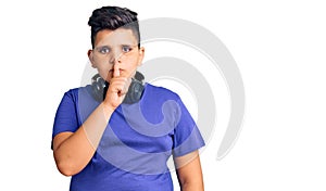 Little boy kid listening to music wearing headphones asking to be quiet with finger on lips
