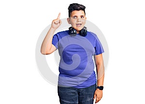 Little boy kid listening to music wearing headphones pointing finger up with successful idea