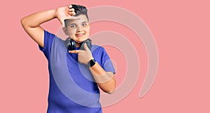 Little boy kid listening to music wearing headphones smiling making frame with hands and fingers with happy face